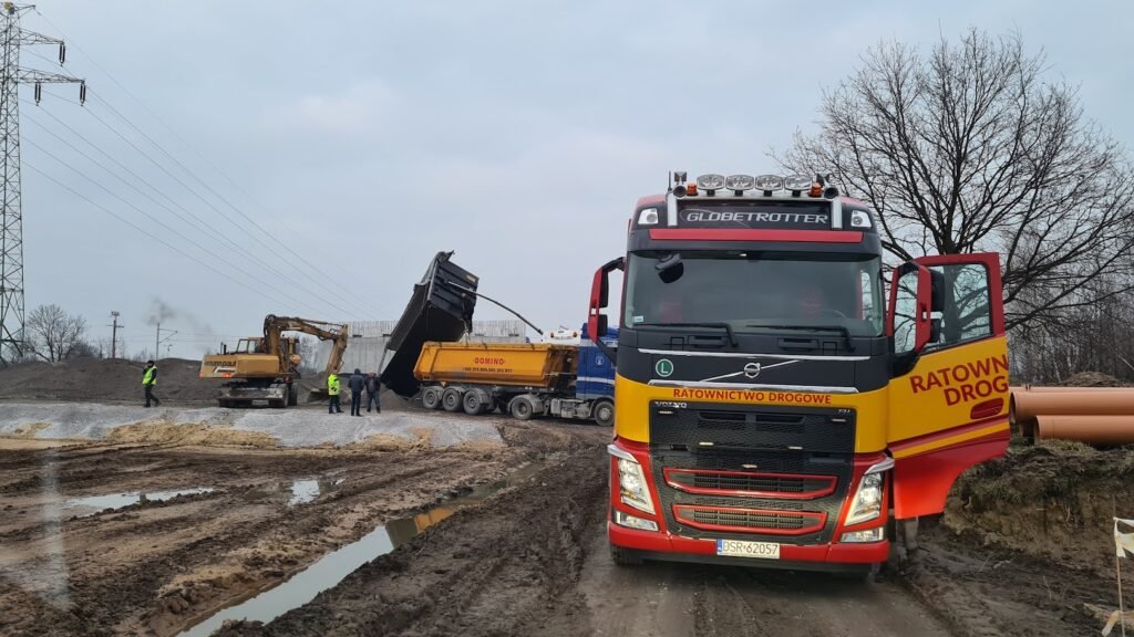 Zdjęcie lawety w Środzie Śląskiej gotowej do transportu uszkodzonego pojazdu na tle malowniczego krajobrazu.